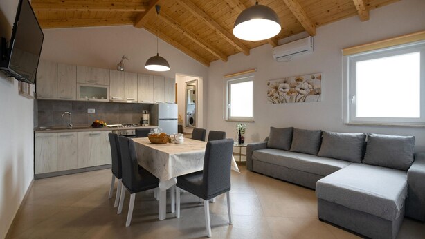 A modern kitchen with a dining area, a gray sofa, and a TV mounted on the wall. - Beautiful home in Orihi with WiFi (Orihi)