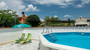 An outdoor swimming pool with a white pool edge, two green lounge chairs, and a blue umbrella. - Beautiful home in Orihi with WiFi (Orihi)