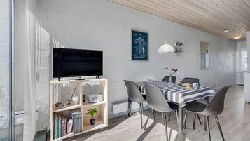 En moderne stue med et fladskærms-tv, spisebord, stole og en reol.