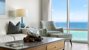A modern living room with a view of the ocean, a glass fishbowl on a wooden table, and a lamp on a side table.