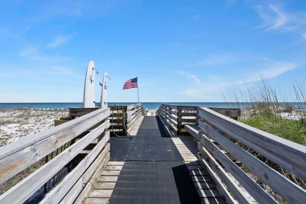 A wooden boardwalk leading to a beach with two surfboards and an American flag.