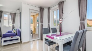 Ett modernt matområde med ett glasbord, grå stolar och en lila kudde på en soffa.