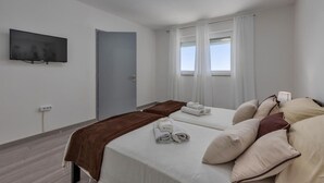 Habitación de hotel con dos camas, un televisor de pantalla plana, una puerta y una ventana con cortinas.