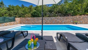 Piscina con paredes de piedra, sillas de descanso y una mesa con bebidas.