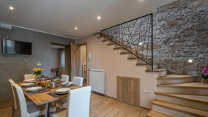 A dining area with a wooden table set for four, white chairs, and a stone wall with a staircase. - Amazing home in Barban (Barban)