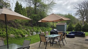 Eine Terrassengruppe im Freien mit Tisch, Stühlen, zwei Sonnenschirmen und einem Grill.