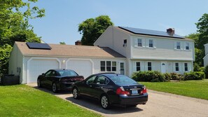 Una casa de dos pisos con un garaje, dos autos estacionados en la parte delantera y paneles solares en el techo.