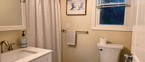 Un baño con lavamanos blanco, inodoro, cortina de ducha y ventana con persianas.