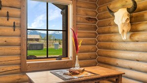 Ein rustikales Holzhütten-Interieur mit Tisch, Stühlen, einem Fenster mit Bergblick und einem Kuhschädel an der Wand.