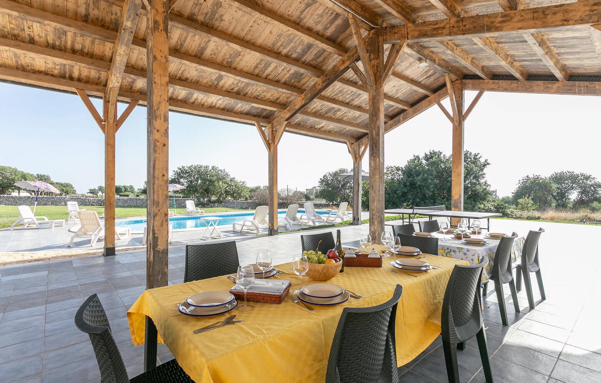 An outdoor dining area with a pool and lounge chairs in the background.