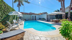A swimming pool with lounge chairs and umbrellas, surrounded by palm trees and a stone wall. - Beach front home in Casuzze-Finaiti with sauna (Casuzze-Finaiti)