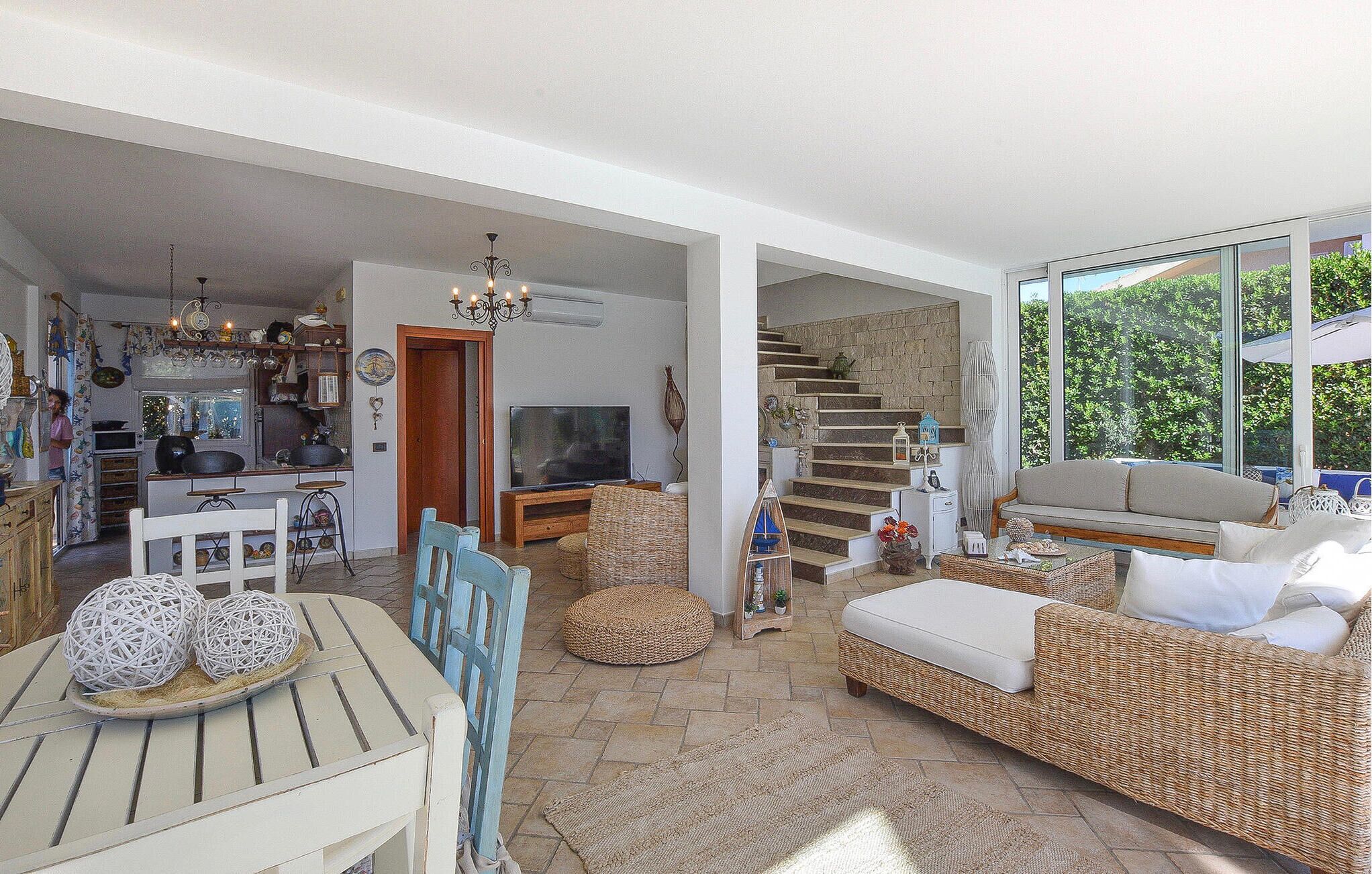 Un vaste espace de vie comprenant une table à manger, des meubles en osier, un téléviseur et un escalier menant à un niveau supérieur.