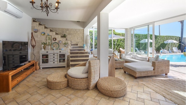 A spacious living area with a TV, wicker furniture, and a view of a swimming pool. - Beach front home in Casuzze-Finaiti with sauna (Casuzze-Finaiti)