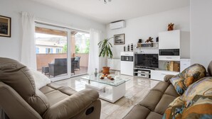 Un salon moderne avec une table basse en verre, des canapés de couleur beige, un téléviseur et une plante en pot.