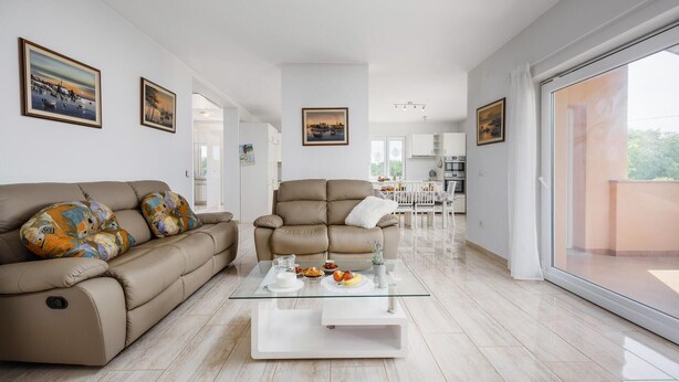 Un salon moderne avec un canapé beige, une table basse en verre et un coin repas comprenant une table et des chaises blanches.