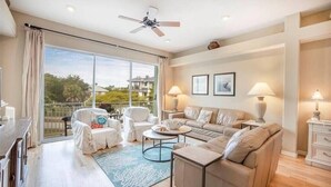 A spacious living room with a large sliding glass door leading to a balcony, a ceiling fan, and a sofa set. - Siesta Sunrise II-Between the Beach and Village (Siesta Key)