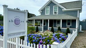 Una casa blu con una staccionata bianca, un cartello con su scritto 'Pipers Shore Cottages' e un giardino con ortensie.