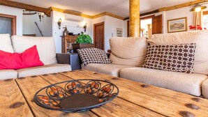 Un salon chaleureux avec une table basse en bois, un canapé beige agrémenté de coussins à motifs et un coussin rouge.