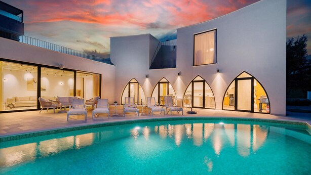 Ein moderner Poolbereich mit klarem, blauem Wasser, weißen Liegestühlen und einem Sonnenuntergangshimmel.