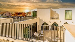 Ein modernes Gebäude mit Balkon, Sitzgelegenheit im Freien und Blick auf den Sonnenuntergang.