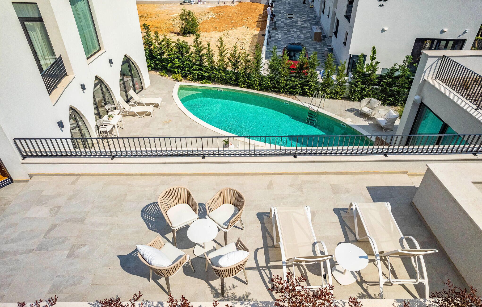Zona de piscina al terrat amb gandules i una taula petita, envoltada d'un edifici de color blanc amb finestres d'arc i una vista despejada de la piscina.