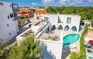 Une villa moderne dotée d’une piscine, d’un espace salon extérieur couvert et offrant une vue sur le quartier environnant.