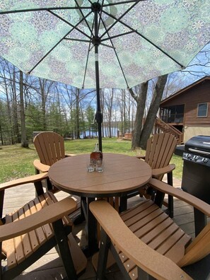 A round wooden table with four chairs, an umbrella, and a grill. - Lakefront, Wooded, & Secluded Home - Family Dogs Welcome. (Oakland)
