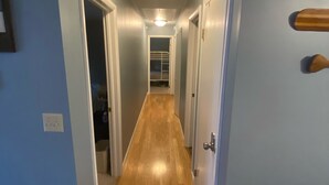 A narrow hallway with wooden flooring and light blue walls, leading to a door with a small wooden panel. - Lakefront, Wooded, & Secluded Home - Family Dogs Welcome. (Oakland)