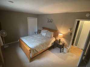 A bedroom with a wooden bed, a nightstand with a lamp, a wall sign, and a door. - Lakefront, Wooded, & Secluded Home - Family Dogs Welcome. (Oakland)