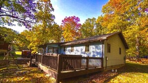 A small cabin with a porch and a fenced yard, surrounded by trees with autumn foliage. - Lakefront, Wooded, & Secluded Home - Family Dogs Welcome. (Oakland)