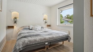 A bedroom with a bed, two wall-mounted lamps, a window with a view, and a small plant on the wall.