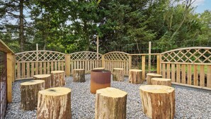 A wooden deck with a metal barrel and round wooden stools arranged in a circle.