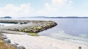 Una zona costera con un rompeolas rocoso, un muelle de madera y una playa de arena.