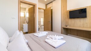 A hotel room with a bed, a TV mounted on the wall, and a bathroom visible through an open door. - Gorgeous home in Peroj (Peroj)