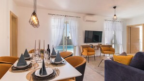 A modern dining area with a table set for four, a TV in the background, and a view of a pool through the windows. - Gorgeous home in Peroj (Peroj)