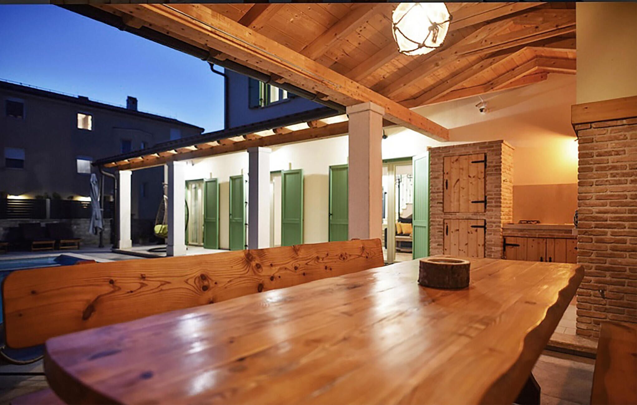 An outdoor wooden table with benches, a brick wall, and a building with green doors in the background.