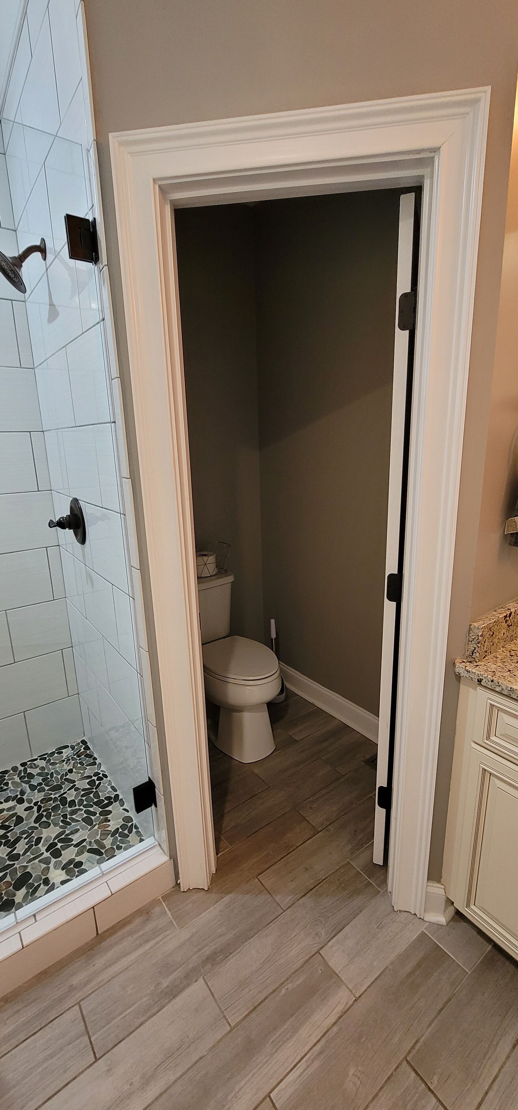 A bathroom with a toilet, a shower with white tiles, and a wooden floor.