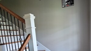 Una scala con gradini in legno e colonne bianche, che conduce a un pianerottolo con tre quadri appesi al muro.