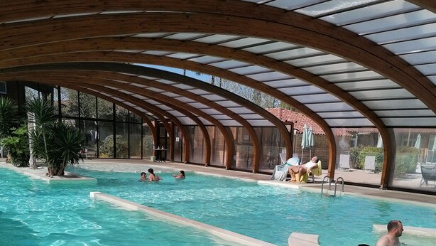 Une grande piscine intérieure dotée d’un plafond en forme d’arche en bois et de panneaux de verre transparent.
