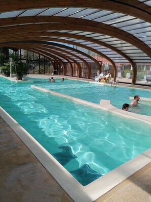 En stor indendørs swimmingpool med et hvælvet træloft og glaspaneler.