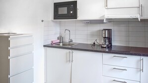 Keittiössä on valkoiset kaapit, musta mikroaaltouuni, kahvinkeitin ja pesuallas.