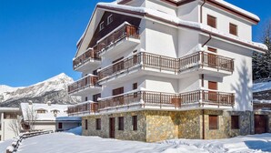A multi-story hotel with balconies, stone foundation, and a mountainous backdrop.