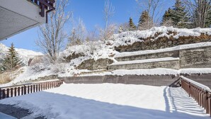 A snow-covered outdoor staircase leading up to a building with a stone wall and a wooden railing.