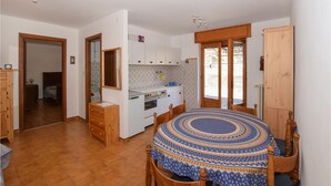 A compact kitchen with white cabinets, a stove, and a sink. There is a dining table with a patterned tablecloth and wooden chairs.