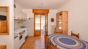 A compact kitchen with a stove, sink, and wooden cabinets. A dining table with a patterned tablecloth is in the center.