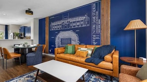 Una sala de estar moderna con un gran mural azul, un sofá de cuero, una mesa de comedor y una mesa auxiliar.