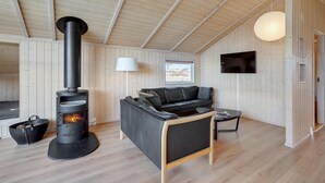 Una habitación acogedora con una estufa de leña, un sofá de cuero y un televisor montado en la pared.