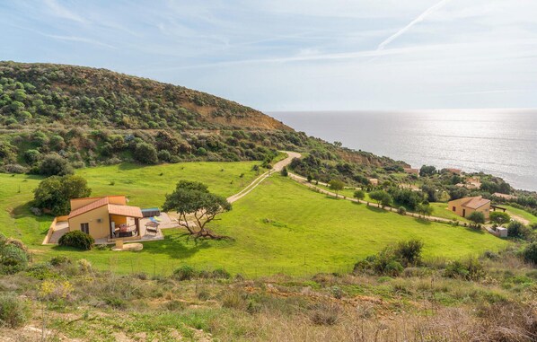 A coastal property with a grassy field, a dirt path, and a building with a red roof.