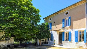 Un edificio tradicional con contraventanas azules, un muro de piedra y un árbol en primer plano.