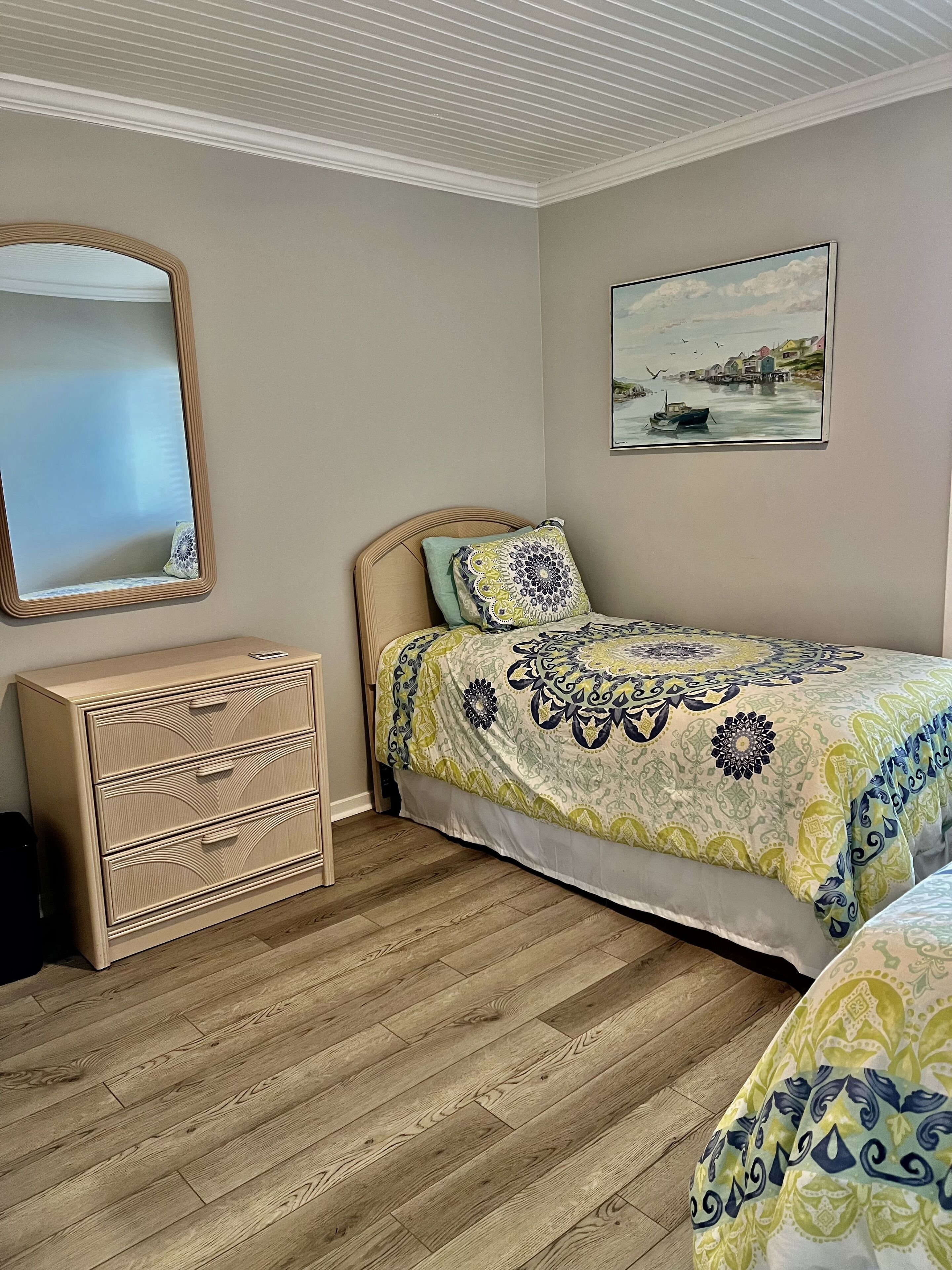 A bedroom with a bed, a dresser, a mirror, and a painting on the wall.